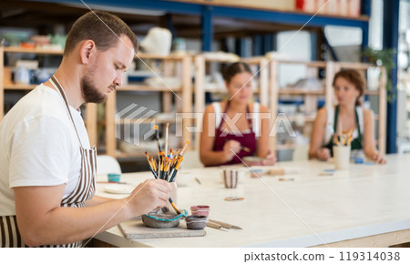 Three craftsperson are busy painting clay products 119314038