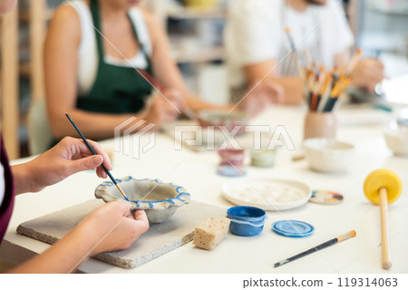 Closeup of female hands painting ceramic plate with paint and brush in pottery workshop 119314063