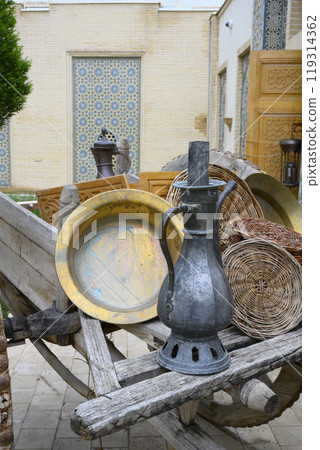 Traditional Uzbek metal jug, plates and wicker baskets in old wooden cart in Samarkand, Uzbekistan 119314362