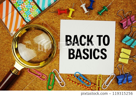 Back To Basics text on paper card with magnifying glass and stationery on cork board background 119315256