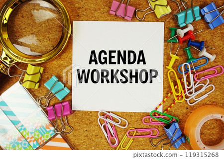 Agenda Workshop text on paper card with magnifying glass and stationery on cork board background 119315268