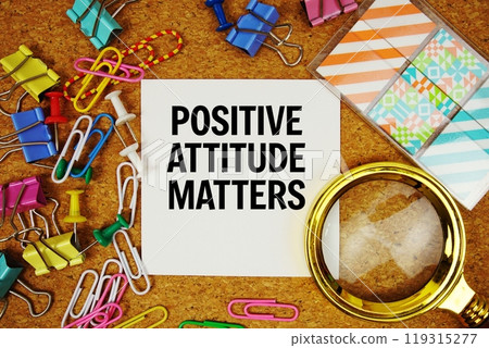 Positive Attitude Matters text on paper card with magnifying glass and stationery on cork board background Positive Attitude Matters text on paper card with magnifying glass and stationery on cork board background 119315277