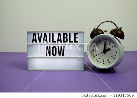 Available Now text on LED lightbox with alarm clock on purple background Available Now text on LED lightbox with alarm clock on purple background 119315509