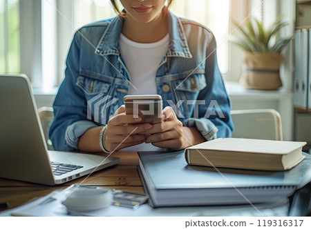 In the room, a woman is seated at a desk and holding a cellphone 119316317