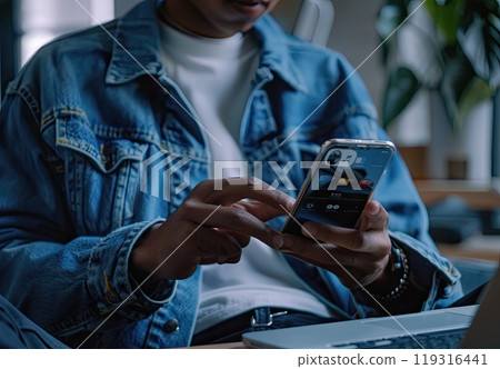 In the room, a woman is seated at a desk and holding a cellphone In the room, a woman is seated at a desk and holding a cellphone 119316441