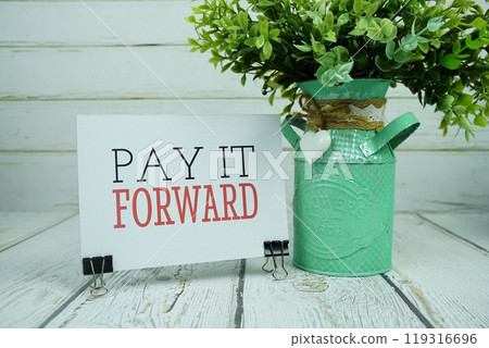 Pay It Forward text message on paper card with alarm clock on wooden background Pay It Forward text message on paper card with alarm clock on wooden background 119316696