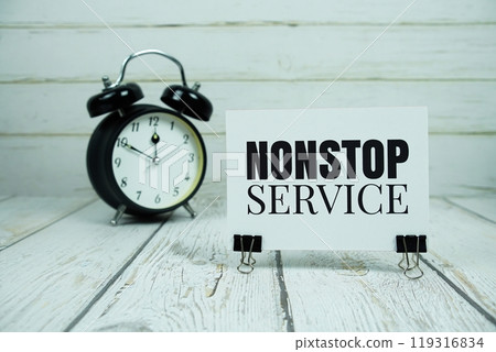 Nonstop Service text message on paper card with alarm clock on wooden background 119316834
