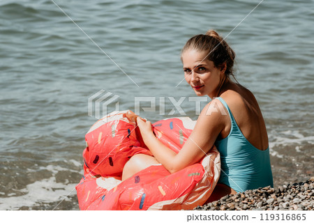 Woman in a Blue Swimsuit Holding a Red Inflatable Ring at the Beach Woman in a Blue Swimsuit Holding a Red Inflatable Ring at the Beach 119316865