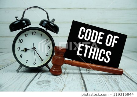 Code of Ethics text on paper card with alarm clock and wooden judge gavel on wooden background 119316944
