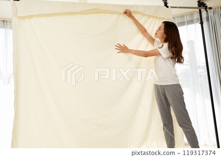 A woman hangs out futon sheets to dry indoors. A woman hangs out futon sheets to dry indoors. 119317374