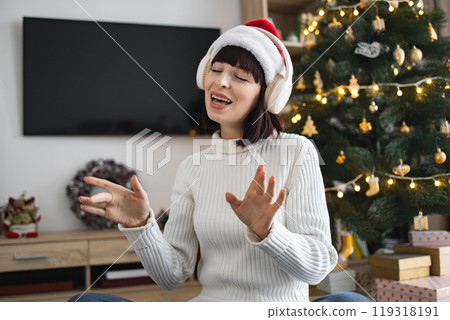 Woman enjoying Christmas music with headphones near decorated tree Woman enjoying Christmas music with headphones near decorated tree 119318191