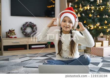 Little girl enjoying music with headphones near Christmas tree 119318194