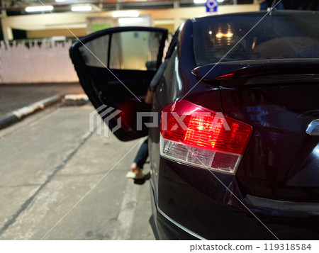parked black car with its rear door open and red brake lights illuminated. The car is parked on a street at night, with some exterior lighting in the background, car on the road, car emergency parked black car with its rear door open and red brake lights illuminated. The car is parked on a street at night, with some exterior lighting in the background, car on the road, car emergency 119318584