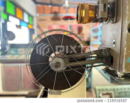 vintage film projector in focus, showcasing a large metal reel with film tightly wound around it, film projector, old cinema equipment, evoking memories of traditional film projection 119318587