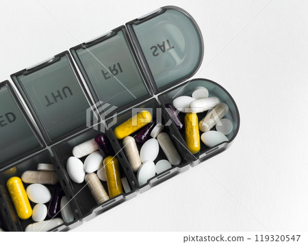 Weekly pill organizer with various capsules and tablets on white background 119320547