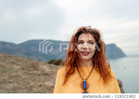 Portrait windswept hair happy woman against a backdrop of mountains and sea. Daylight illuminates the tranquil outdoor setting 119321902