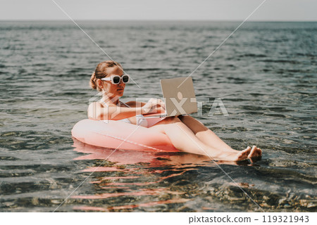 A woman is floating in a pink inflatable raft with a laptop in her hand. She is smiling and she is enjoying her time in the water. A woman is floating in a pink inflatable raft with a laptop in her hand. She is smiling and she is enjoying her time in the water. 119321943