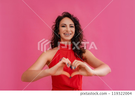 A woman in a red dress is smiling and holding her hands together to make a heart shape. Concept of love and happiness. 119322004