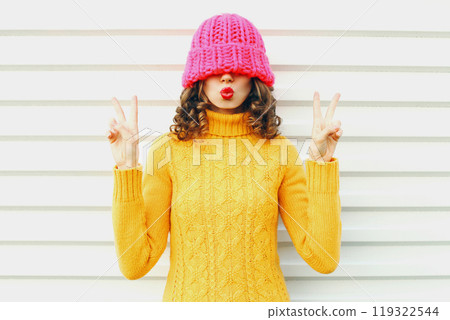 Fashion happy woman blowing kiss, colorful knitted pink hat, yellow sweater over white background Fashion happy woman blowing kiss, colorful knitted pink hat, yellow sweater over white background 119322544