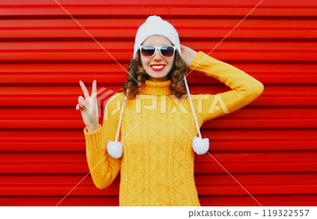 Fashion smiling young woman wearing colorful knitted yellow sweater over red background Fashion smiling young woman wearing colorful knitted yellow sweater over red background 119322557