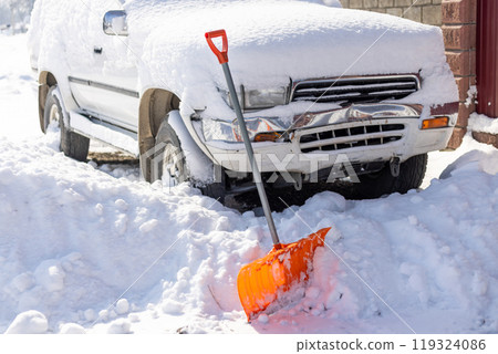orange snow shovel sticking out from snowdrift in front of snow covered white SUV car 119324086