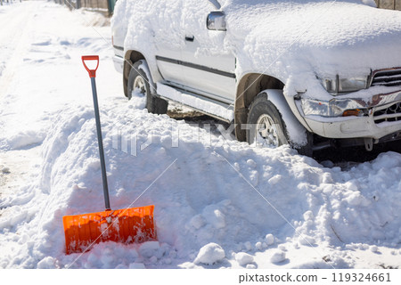 orange snow shovel sticking out from snowdrift in front of snow covered white SUV car orange snow shovel sticking out from snowdrift in front of snow covered white SUV car 119324661