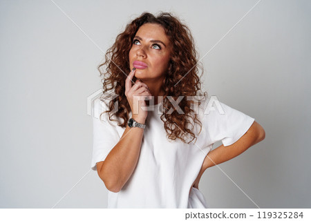 Woman with curly hair thoughtfully pondering in a neutral setting 119325284