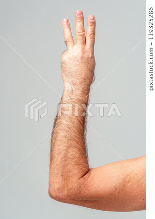Hand gesture indicating the number three against a plain background 119325286