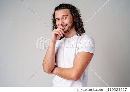 A young man stands thoughtfully against a plain background, expressing contemplation 119325317