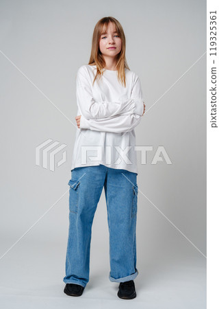 Young woman with long hair in a white sweatshirt standing against a light gray background Young woman with long hair in a white sweatshirt standing against a light gray background 119325361