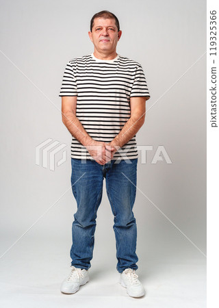 A man stands confidently in a striped shirt, casual jeans with a neutral background A man stands confidently in a striped shirt, casual jeans with a neutral background 119325366