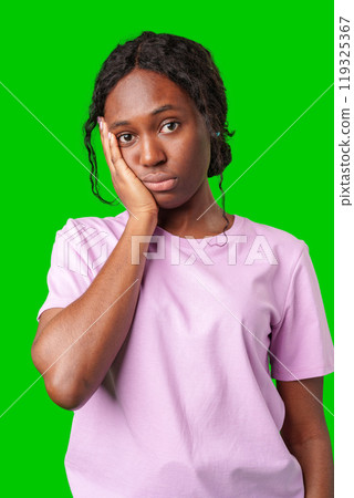A young woman looking thoughtful while standing against a bright green background 119325367