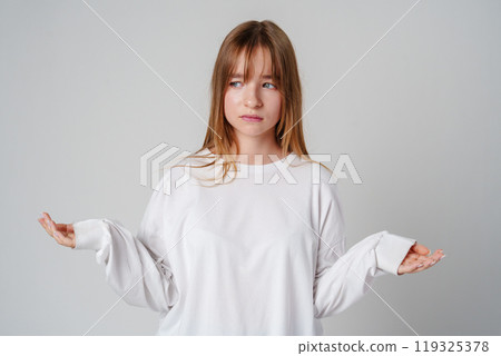 A young girl wearing a white long-sleeve shirt expressing confusion in a minimalistic gray studio setting A young girl wearing a white long-sleeve shirt expressing confusion in a minimalistic gray studio setting 119325378