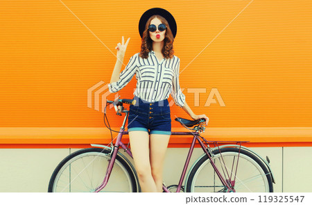 Summer colorful portrait of beautiful young woman with bicycle blowing kiss on orange background 119325547
