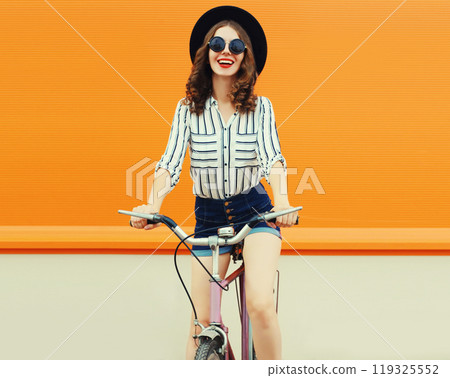 Summer colorful portrait of happy smiling young woman with bicycle in the city on orange background 119325552