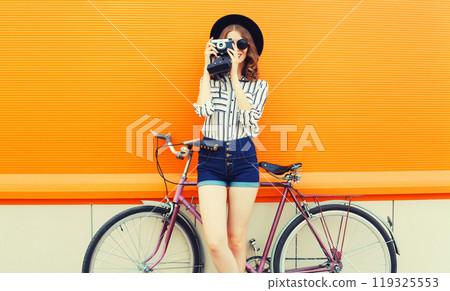 happy young woman photographer taking a picture by camera with bicycle in city on orange background happy young woman photographer taking a picture by camera with bicycle in city on orange background 119325553