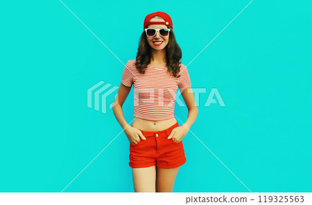 Summer portrait of happy smiling young woman wearing baseball cap, red shorts on blue background Summer portrait of happy smiling young woman wearing baseball cap, red shorts on blue background 119325563
