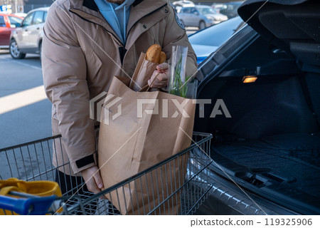 Man Loading Groceries into Car Trunk 119325906
