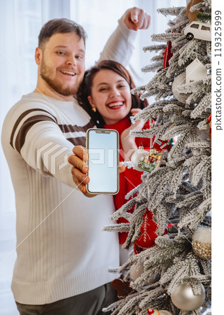man with woman holding phone with empty screen standing near christmas tree man with woman holding phone with empty screen standing near christmas tree 119325999
