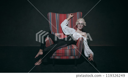 Young man with pale face with lipstick marks on face, leans back with bottle, creating amusing vibe of party aftermath in baroque setting. 119326249