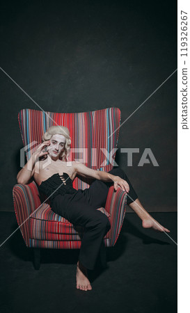 Laid back in bold, colorful armchair, historical character juxtaposes modern furniture with historical character, creating eclectic artistic vision. 119326267