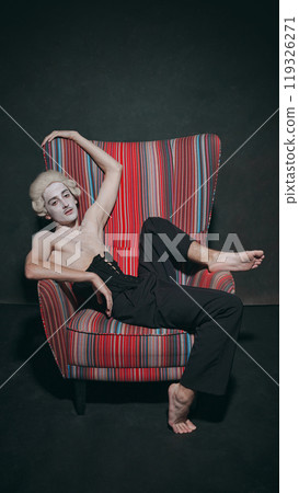 Portrait of young man, dressed old garments, sitting, in relaxed posture in chair against vintage background. History and high fashion. 119326271