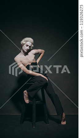 Portrait of young man elegantly leaning on chair, lends historical poise with modern calm, creating balance between art and fashion. 119326275