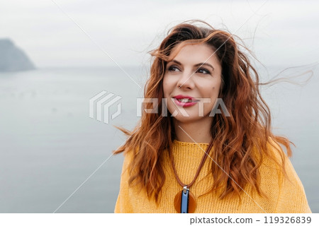 Portrait windswept hair happy woman against a backdrop of mountains and sea. Daylight illuminates the tranquil outdoor setting 119326839
