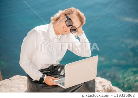 Business woman on nature in white shirt and black skirt. She works with an iPad in the open air with a beautiful view of the sea. The concept of remote work. 119326868