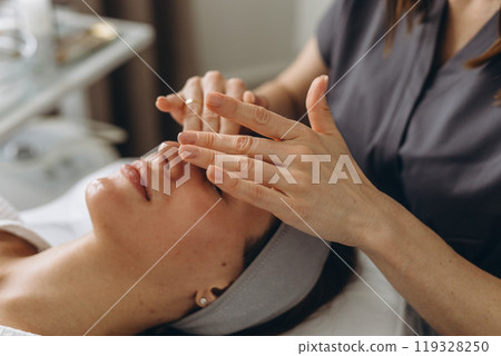 A beautiful woman enjoys a facial massage at a spa salon,indulging in skin and body care treatments. A beautiful woman enjoys a facial massage at a spa salon,indulging in skin and body care treatments. 119328250