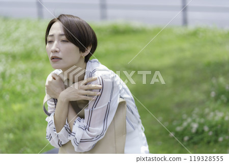 Middle-aged woman sitting on a park bench with her arms folded Middle-aged woman sitting on a park bench with her arms folded 119328555