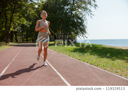 A Woman Jogging on a Beautiful Scenic Track Adjacent to the Serene Water Landscape 119329513