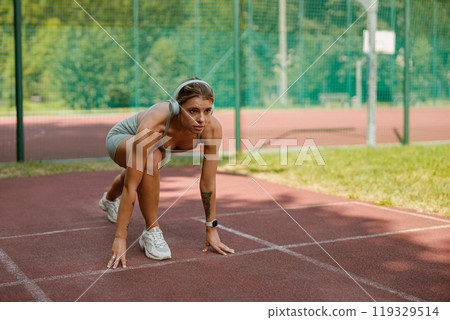 An athletic woman prepares to sprint on the track, showcasing her determination and strength 119329514
