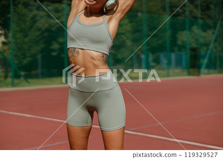 A Fit and Energetic Woman Stretching on a Tennis Court, Dressed in Trendy Stylish Activewear A Fit and Energetic Woman Stretching on a Tennis Court, Dressed in Trendy Stylish Activewear 119329527